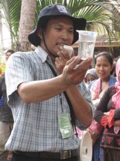 Solihin asks the crowd whether anyone wants to drink a cup of feces-contaminated water.