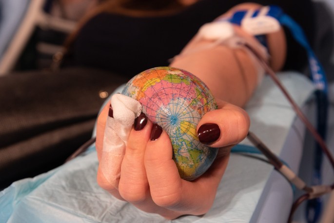 A femme-presenting hand squeezes a globe stress ball while the individual donates blood.